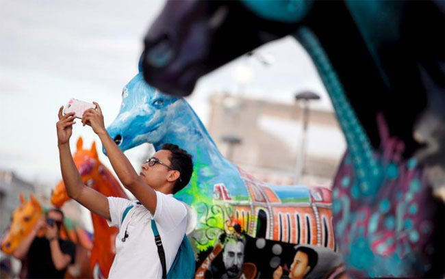 游客们拿出手机与玻璃纤维马自拍合影